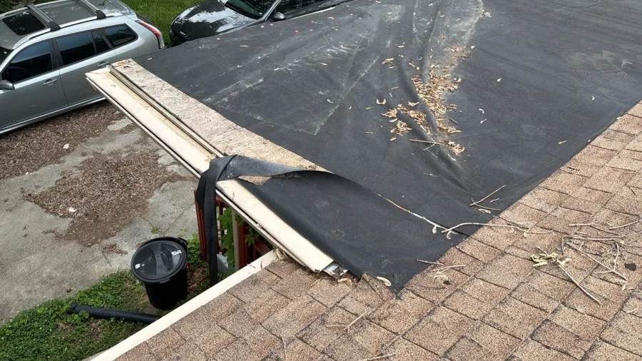 Storm-damaged roof edge with torn underlayment and loose roofing material